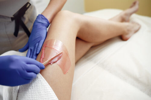Profissional com luvas a depilar a perna de uma cliente, num espaço de estética.