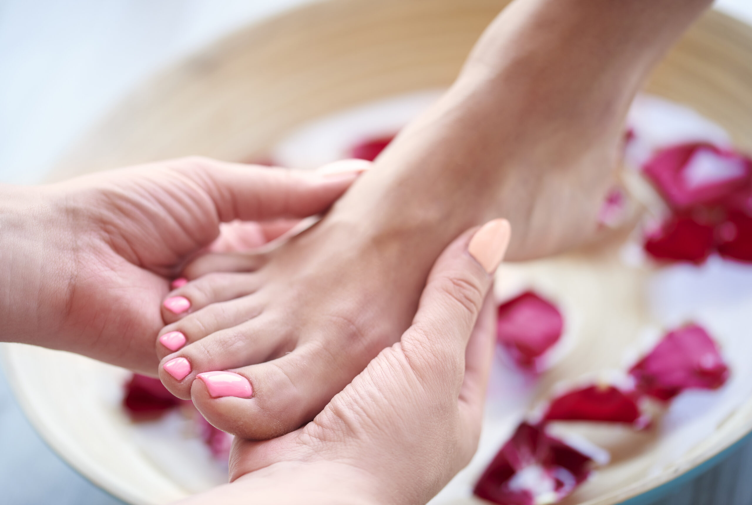 Pés com as unhas pintadas em tom rosa após uma pedicure, junto a uma taça de água com pétalas.
